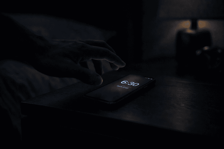 main qui attrape un téléphone allumé comme réveil sur table de nuit chambre nuit