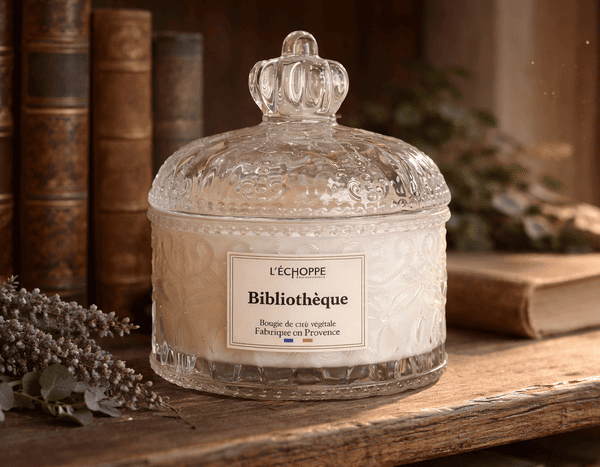 Bougie parfumée Bibliothèque L'Échoppe Buissonnière posée sur une étagère en bois avec des livres anciens et de la lavande