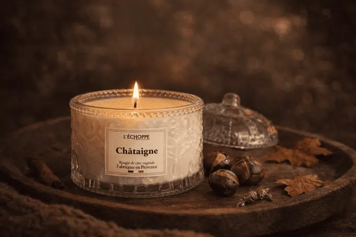 Bougie parfumée à la Châtaigne de L'Échoppe Buissonnière allumée sur un plateau en bois avec des châtaignes et des feuilles mortes