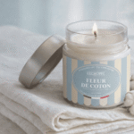 Bougie parfumée Fleur de Coton de L'Échoppe Buissonnière allumée sur un linge blanc avec des fleurs de coton