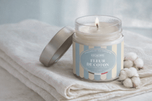 Bougie parfumée Fleur de Coton de L'Échoppe Buissonnière allumée sur un linge blanc avec des fleurs de coton