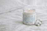 Bougie parfumée Fleur de Coton de L'Échoppe Buissonnière allumée sur un drap blanc avec des fleurs de coton