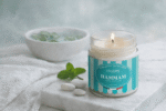 Bougie parfumée Hammam de L'Échoppe Buissonnière allumée sur un plan de marbre avec des feuilles de menthe et des galets blancs