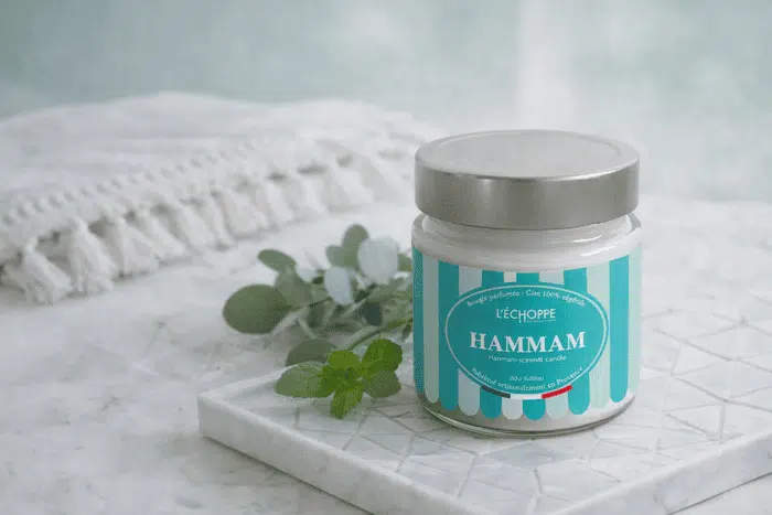 Bougie parfumée Hammam de L'Échoppe Buissonnière avec couvercle posée sur un plateau en marbre avec des branches d'eucalyptus et de menthe