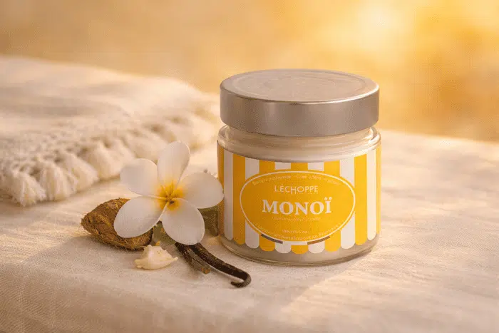 Bougie parfumée Monoï de L'Échoppe Buissonnière avec couvercle posée sur un tissu en lin avec une fleur de tiaré et une gousse de vanille