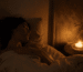 Femme allongée dans un lit douillet pratiquant la respiration 4-7-8, main posée sur la poitrine, bougie allumée sur la table de chevet