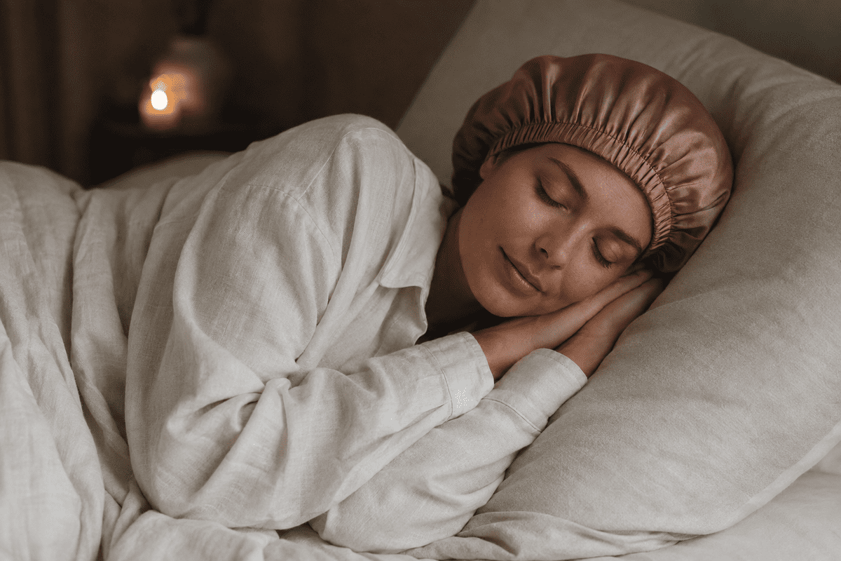 Femme endormie portant un bonnet de nuit en satin rose poudré sur un oreiller en lin ivoire