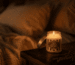 Bougie dans la chambre allumée sur une table de chevet en bois, lumière ambrée tamisée