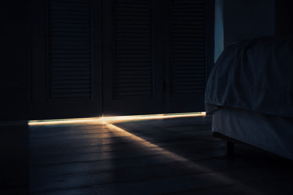 Lame de lumière de l'aube filtrant sous les volets d'une chambre plongée dans l'obscurité