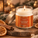 Bougie parfumée Cannelle Orange L'Échoppe Buissonnière allumée sur un plan en bois avec des bâtons de cannelle et des tranches d'orange séchée