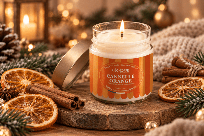 Bougie parfumée cannelle orange échoppe buissonnière allumée Bougie parfumée Cannelle Orange L'Échoppe Buissonnière allumée sur un plan en bois avec des bâtons de cannelle et des tranches d'orange séchée