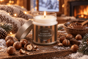 Bougie parfumée Noisette Gourmande L'Échoppe Buissonnière allumée sur un plan en bois avec des noisettes entières et concassées