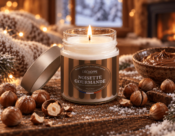 Bougie parfumée Noisette Gourmande L'Échoppe Buissonnière allumée sur un plan en bois avec des noisettes entières et concassées