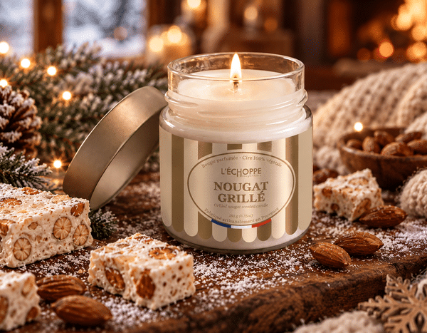 Bougie parfumée Nougat Grillé L'Échoppe Buissonnière allumée sur un plan en bois avec des amandes et des morceaux de nougat