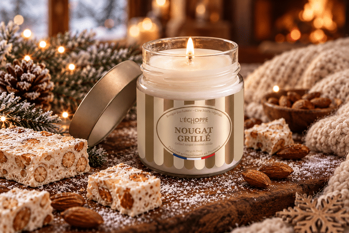 Bougie parfumée Nougat Grillé L'Échoppe Buissonnière allumée sur un plan en bois avec des amandes et des morceaux de nougat