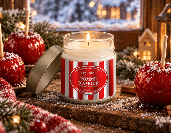 Bougie parfumée Pomme d'Amour L'Échoppe Buissonnière allumée sur un plan en bois avec des pommes rouges et des éclats de caramel