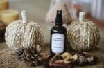 Brume végétale Pomme Cannelle Atelier Louis en flacon verre ambré avec vaporisateur noir, entourée de citrouilles en fibres naturelles, pomme de pin, cannelle et pommes séchées dans une lumière douce